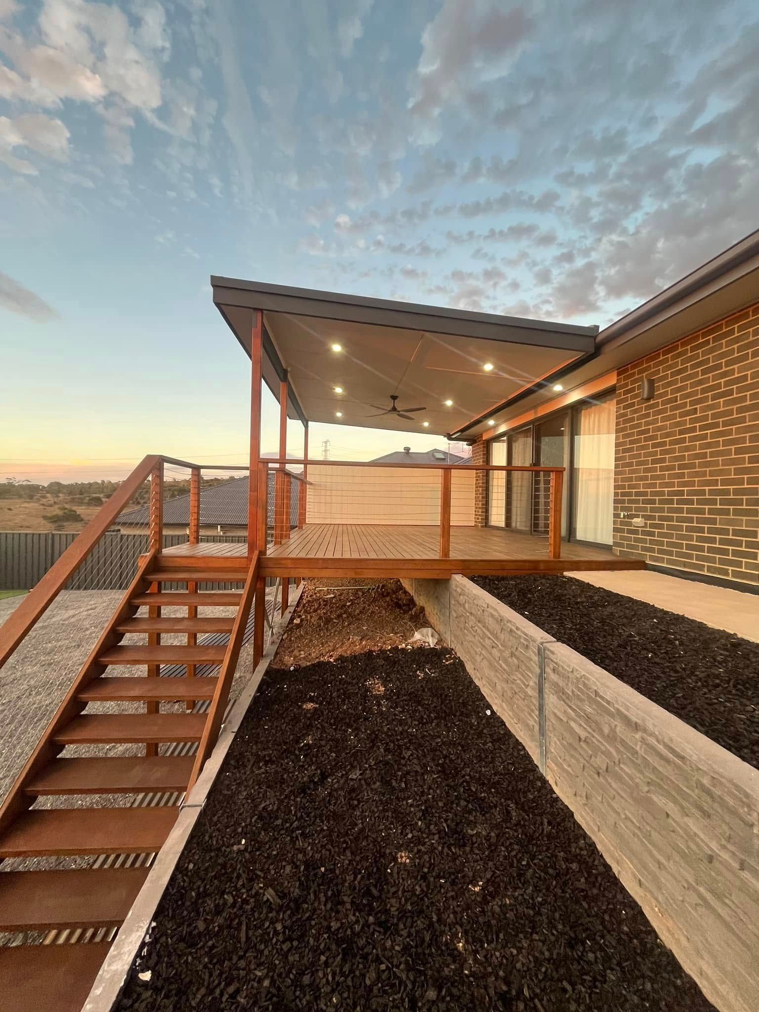 Modern home exterior with a horizontal wooden fence, stone landscaping, and the address number 26 visible on the wall.