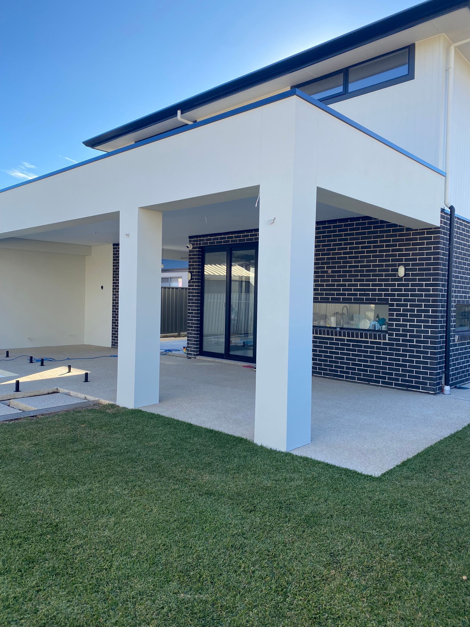 A modern patio with white columns and outdoor furniture overlooks a grassy yard and nearby water under a cloudy sky.