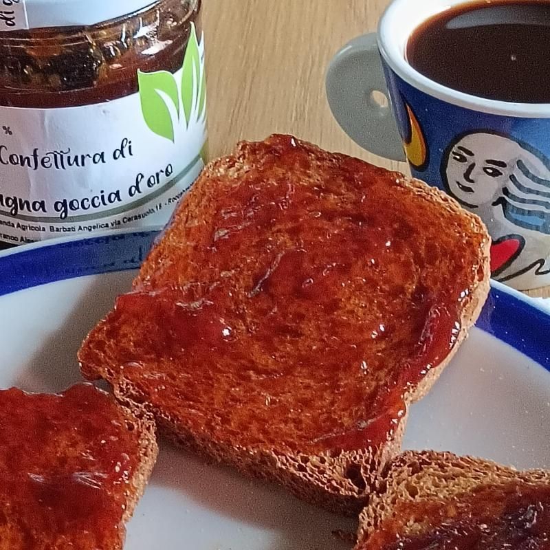 Pane tostato con marmellata accanto a un vasetto di marmellata di pesche e una tazza di caffè su un piattino.