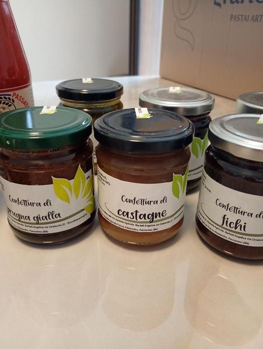 Cinque piccoli vasetti di marmellata su un piano di lavoro, etichettati con le varietà di frutta e con coperchi verdi, neri e argentati.