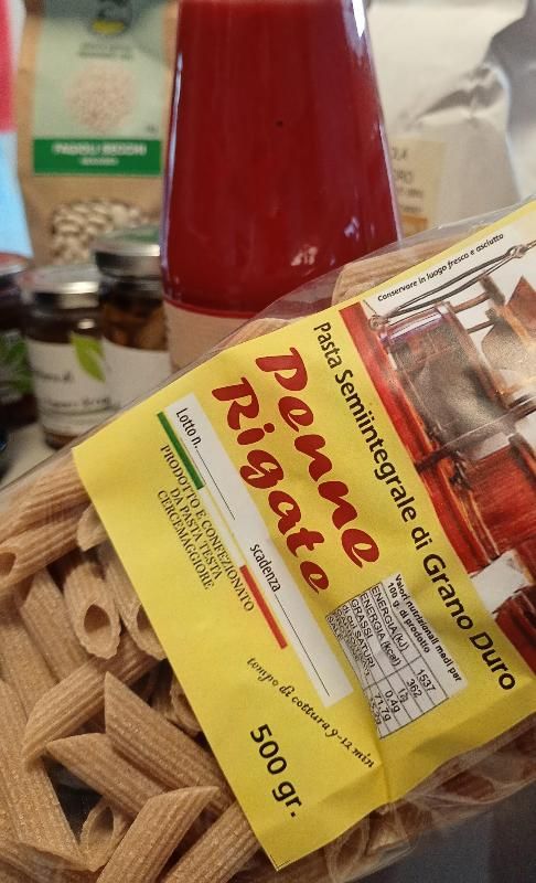Un cestino con la pasta e una bottiglia di salsa rossa accanto a una confezione gialla con la scritta 