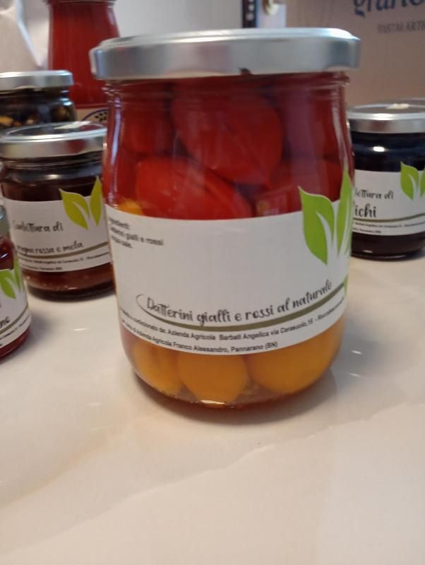 Barattoli di peperoni rossi e pomodori gialli conservati con etichette bianche su un tavolo