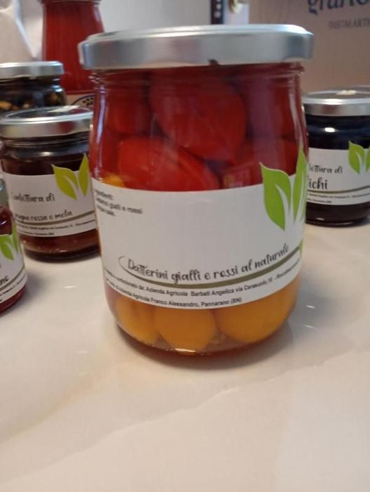 Barattoli di peperoni rossi e pomodori gialli conservati con etichette bianche su un tavolo