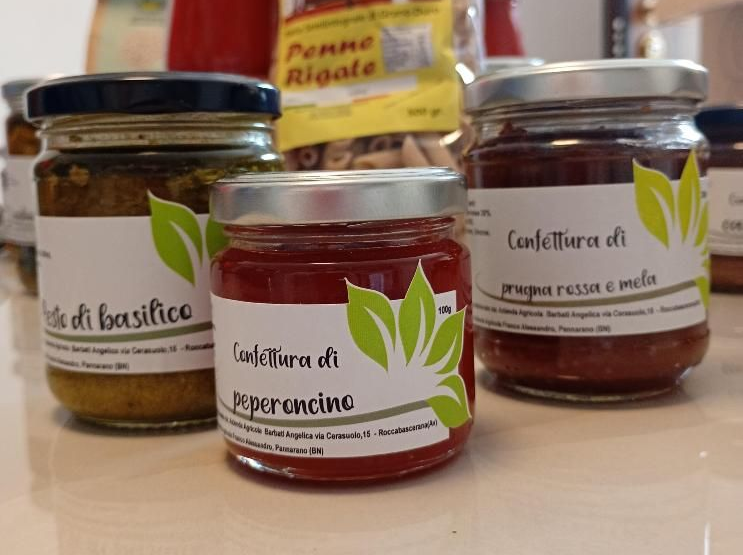 Su un bancone, tre barattoli di salse spalmabili italiane con etichette al basilico, al peperoncino e rosso-arancio.