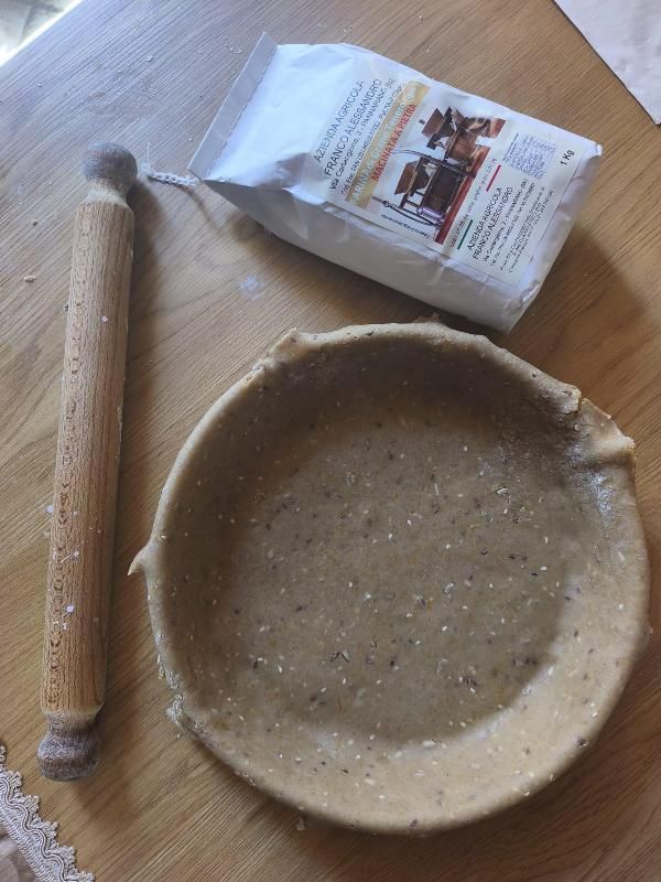 Un cucchiaio di legno, una ciotola di ceramica e un sacchetto di preparato in polvere su un tavolo di legno.