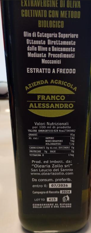 Primo piano di una bottiglia di vetro nero con etichetta italiana dorata, probabilmente olio d'oliva, su sfondo blu.