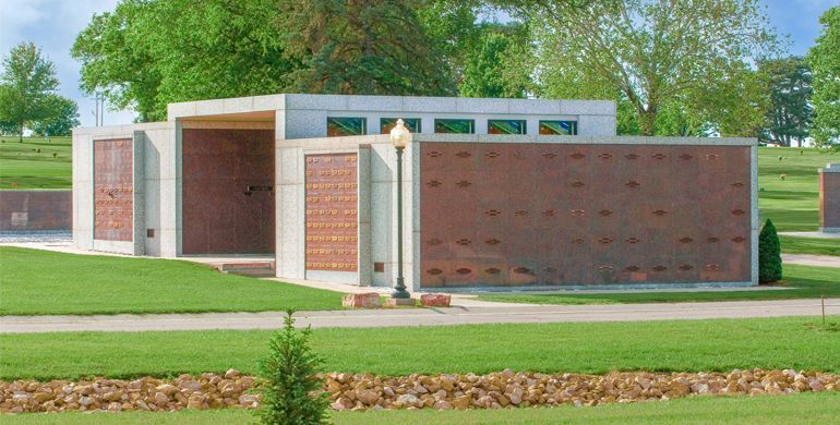Modern brick building with a flat roof and large windows, set on a grassy lawn with trees behind it