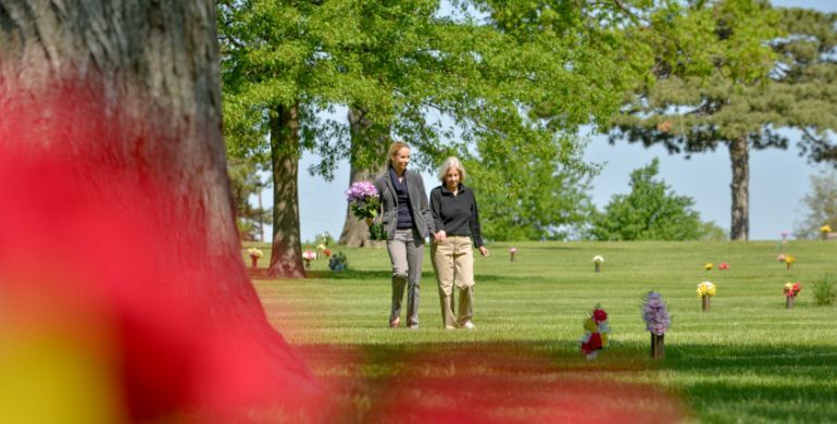 Two people walking on a grassy lawn with trees and small figures in the distance