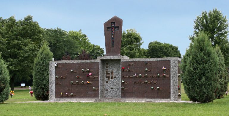 Brick memorial wall with plaques in a green park, topped by a central cross-like monument