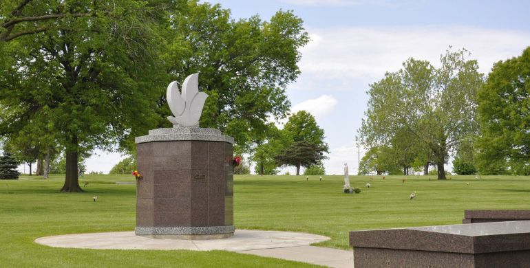 White sculpture on a stone pedestal in a green park with trees and open lawn