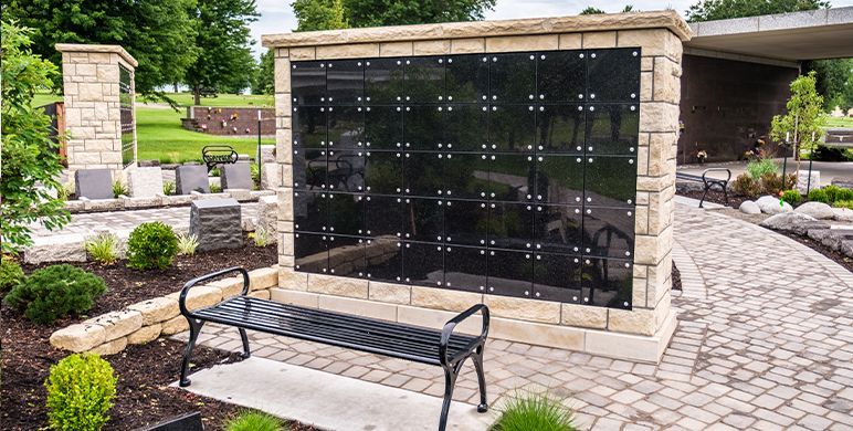 Outdoor memorial wall with black plaques and a bench in a landscaped courtyard
