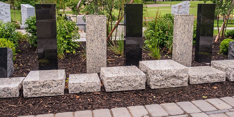 Stone memorial plaques and upright markers in a landscaped garden with greenery behind them