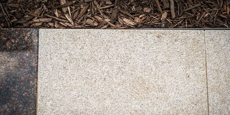 Light beige stone pavers bordered by dark mulch and a patch of concrete