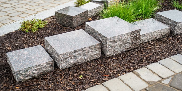 Granite stepping stones in a landscaped garden bed with mulch and small green plants