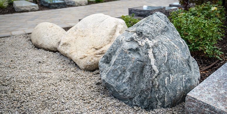 Large decorative boulders on a gravel landscaped path beside green shrubs.