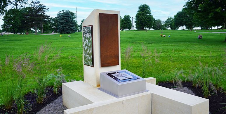 Outdoor memorial sculpture in a green field, with a white stone pedestal and bronze panel.