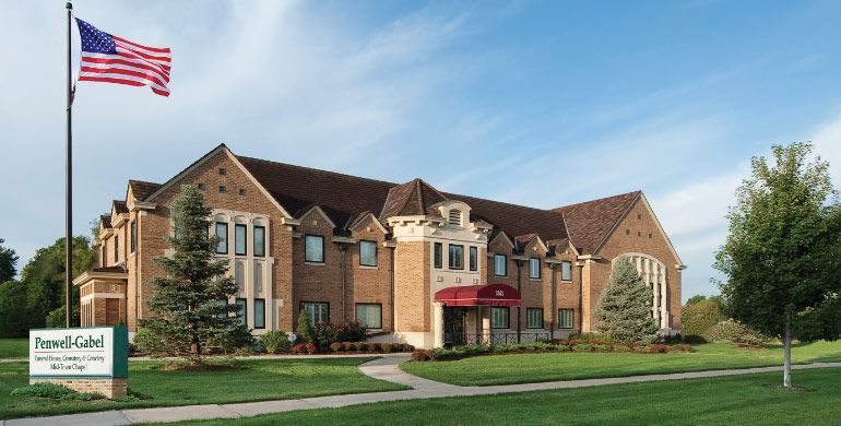 Brick apartment building with red awnings, green lawn, and an American flag by the entrance