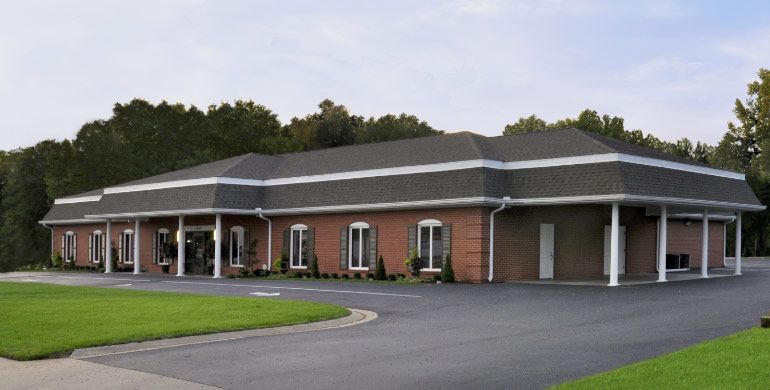 Single-story brick office building with white columns and a dark roof, viewed from a parking lot.