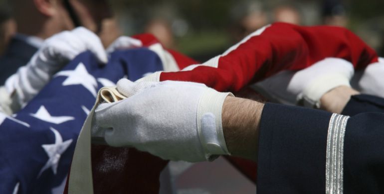 Gloved hands folding a U.S. flag at a funeral ceremony