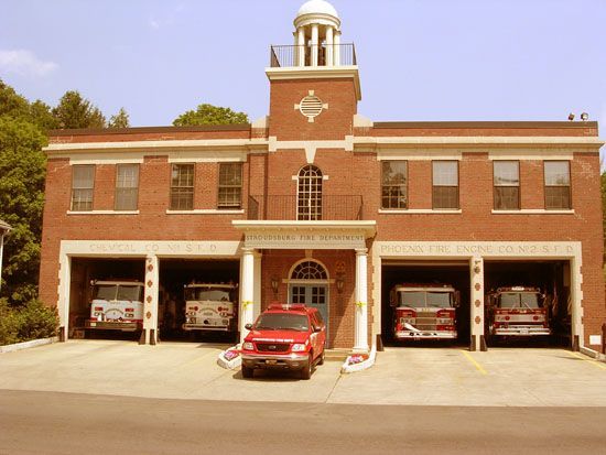 Brick fire station with four open bays, fire trucks inside, and a red pickup truck parked in front.