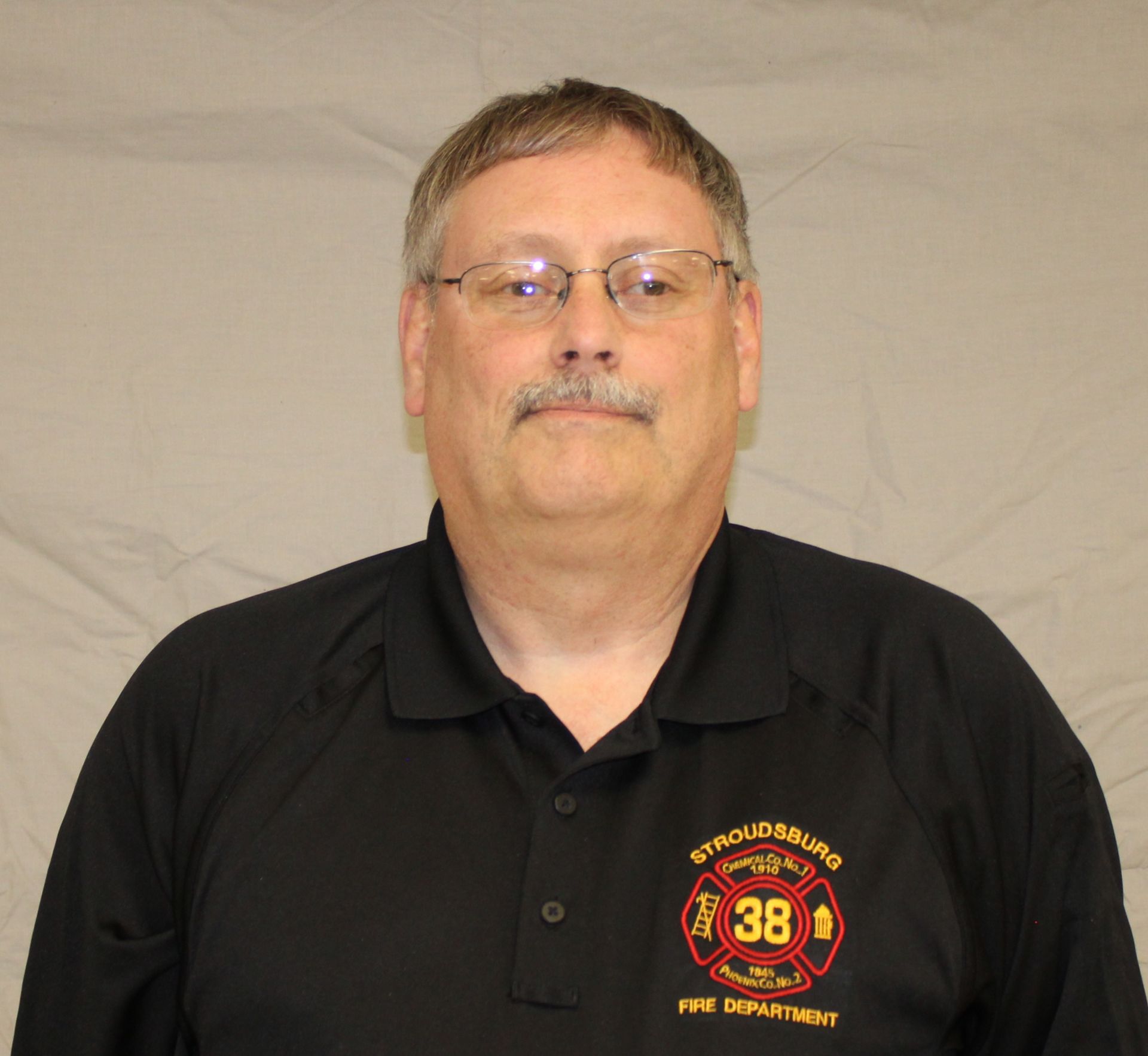 A man wearing glasses and a black shirt with a Stroudsburg Fire Department logo, looking at the camera.