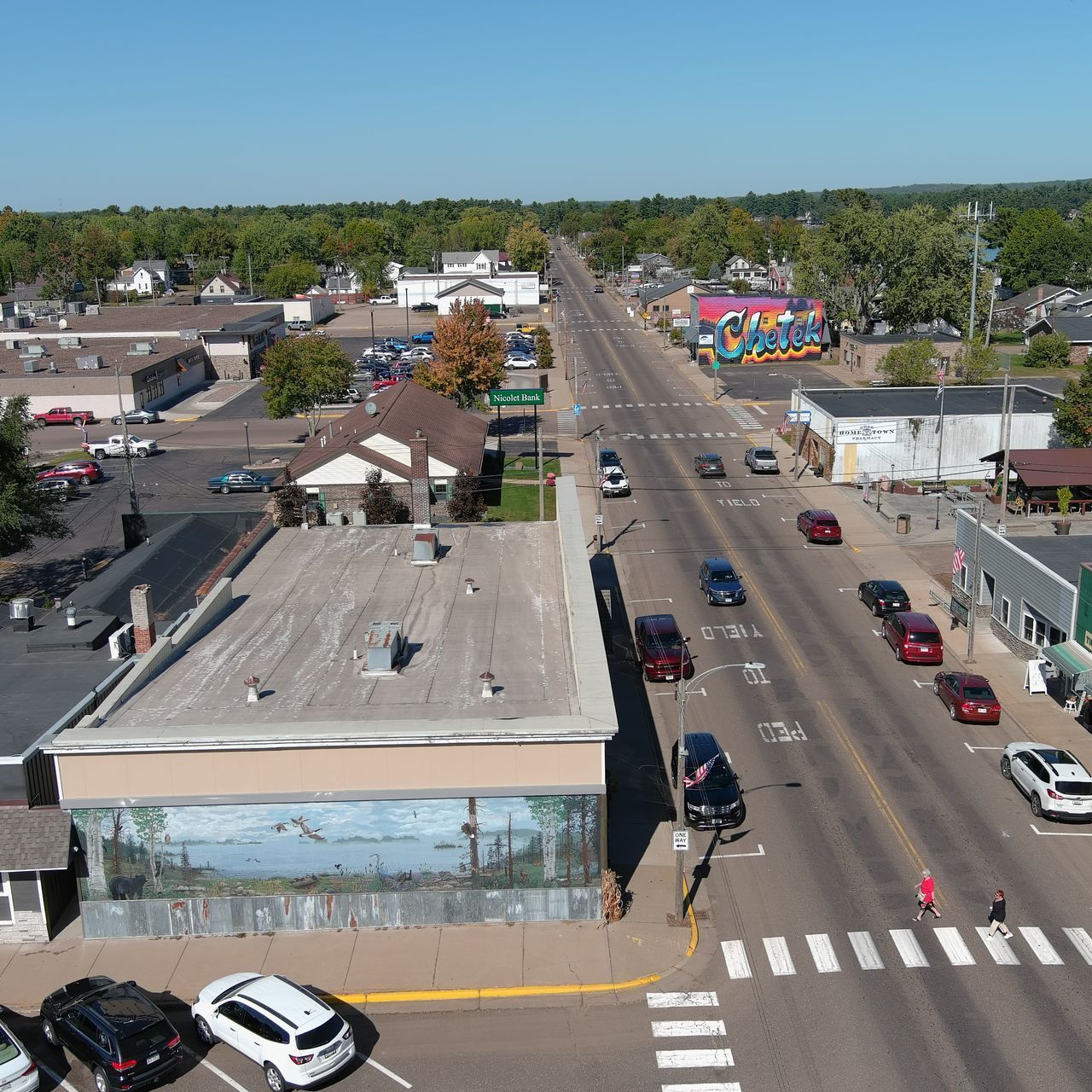 Aerial view of a town street lined with businesses and cars on a sunny day.