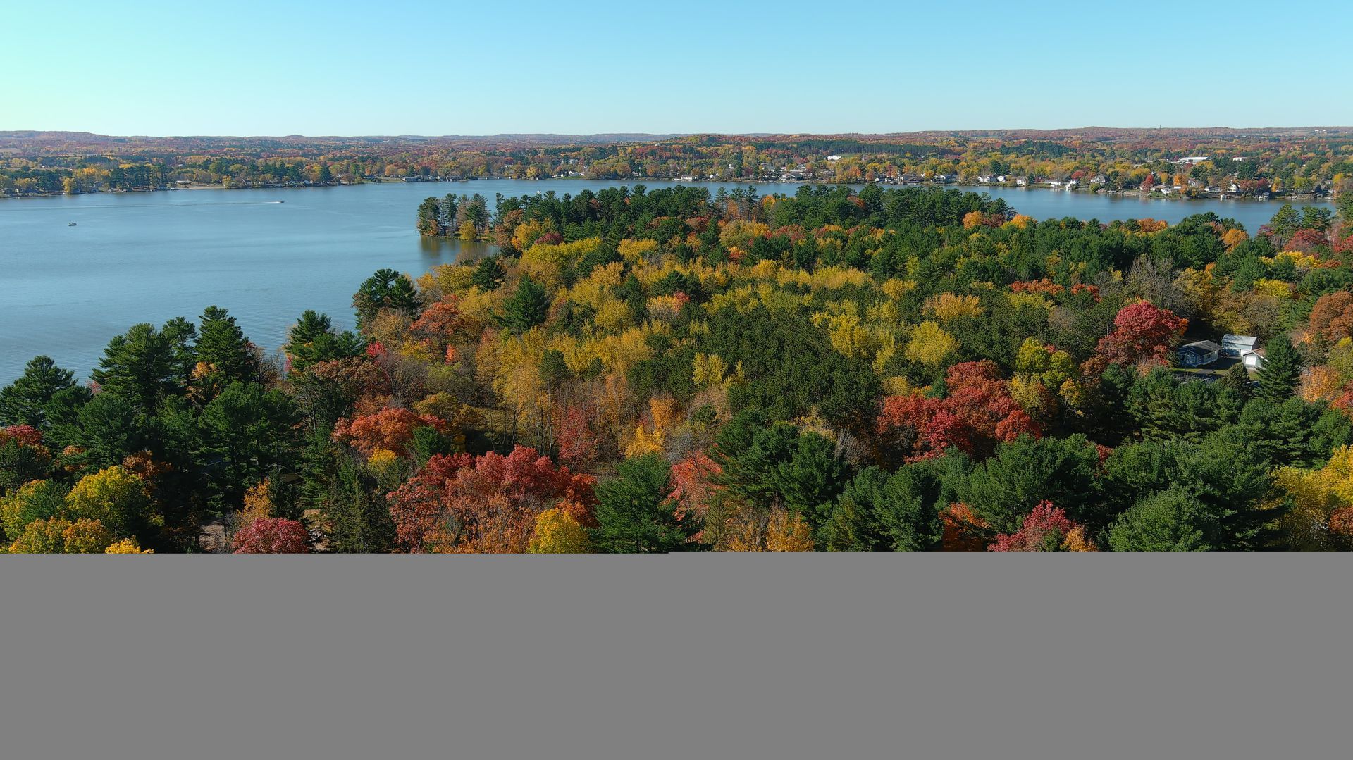 Vibrant fall foliage surrounds a calm lake under a clear blue sky.