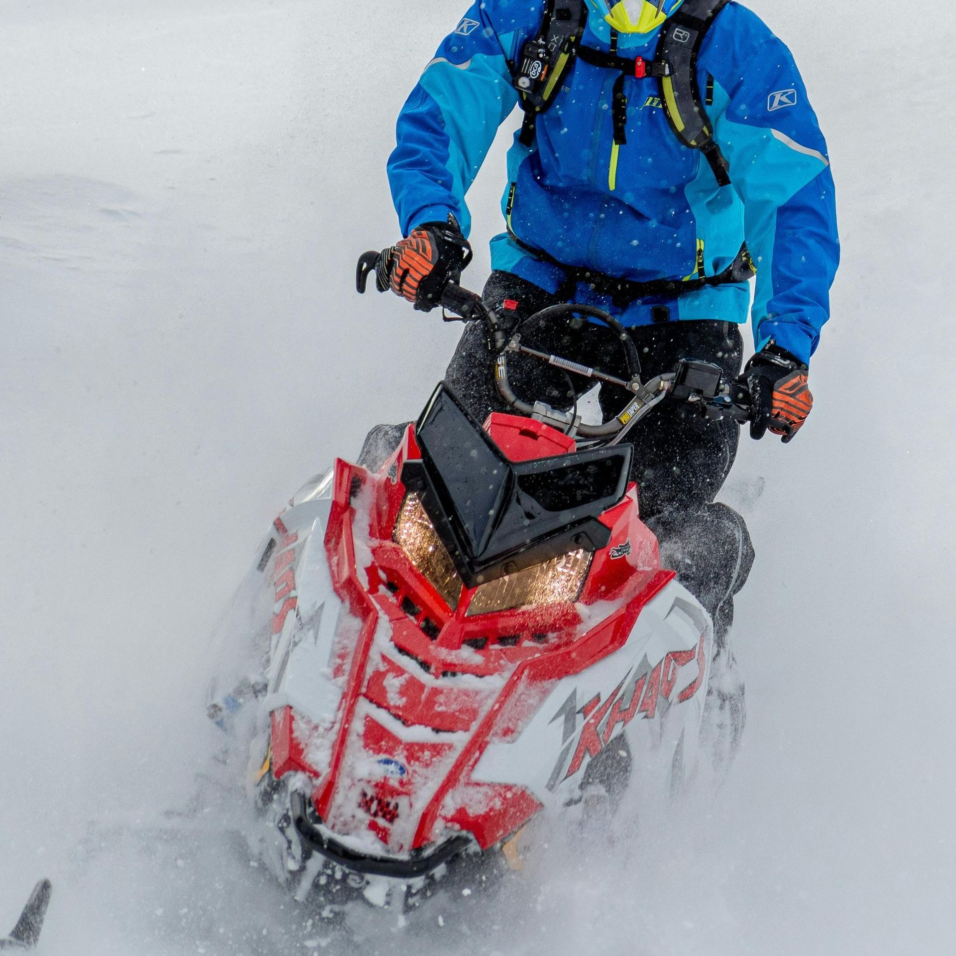 Person rides a red and white snowmobile in snow.