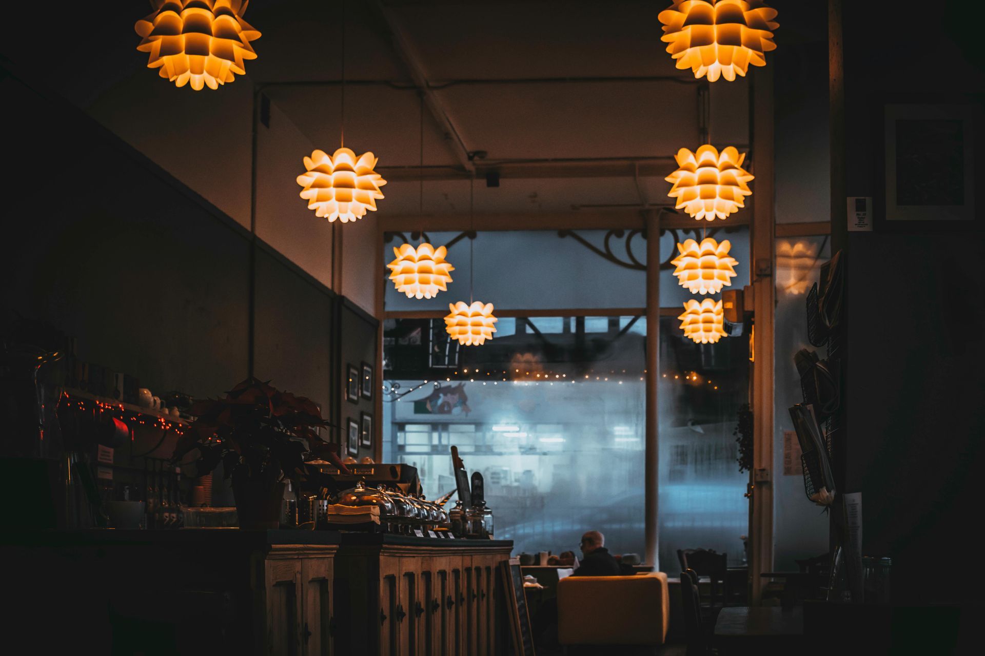 Warmly lit interior with globe-shaped hanging lamps. A dimly lit bar area with a view of a city street.
