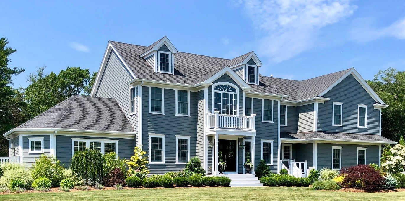 Large blue-gray suburban house with white trim, dormers, and a manicured lawn