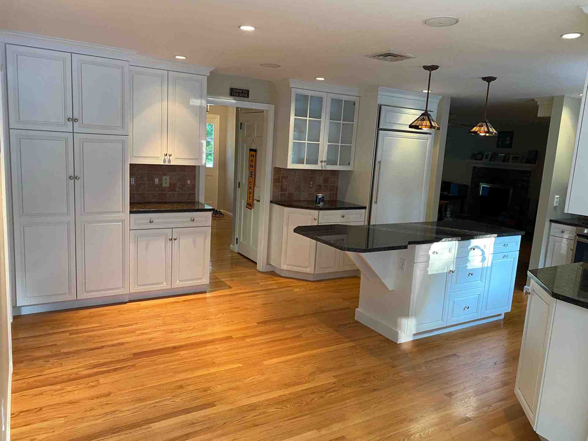 Bright kitchen with white cabinets, hardwood floors, dark island, and stainless steel appliances.