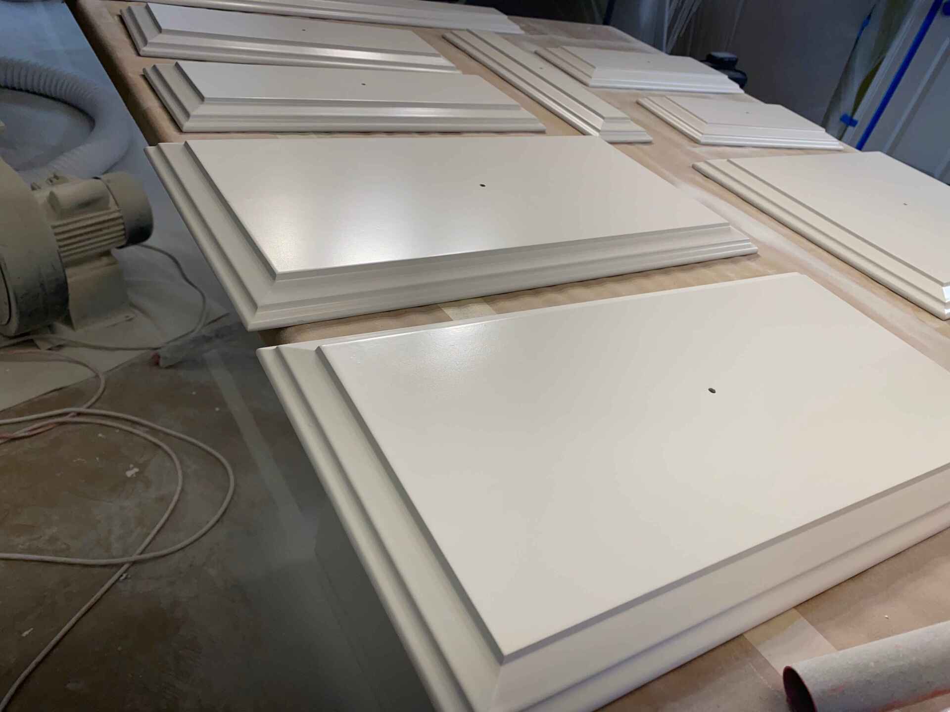 White cabinet doors and panels stacked on a workbench in a workshop