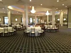 Empty banquet hall with round tables, chairs, and hanging pendant lights under a patterned carpeted floor
