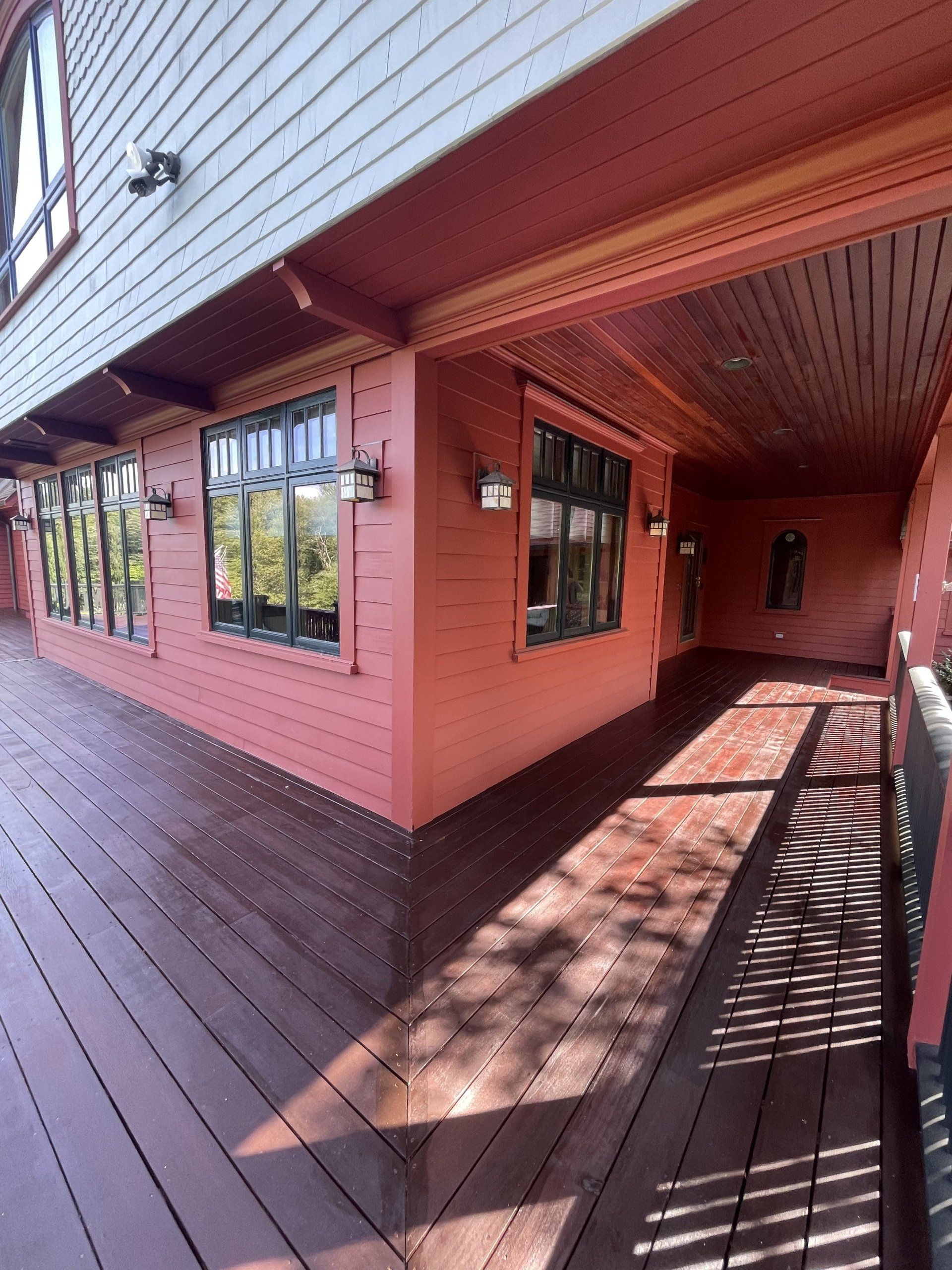 Covered wooden porch with pink walls, windows, and a dark railing in bright sunlight