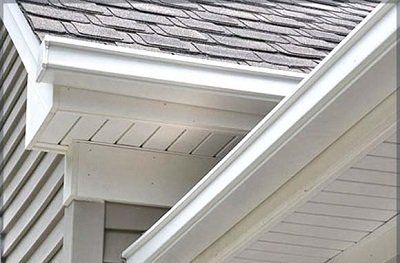 Close-up of a house roof and white gutters with gray shingles and siding