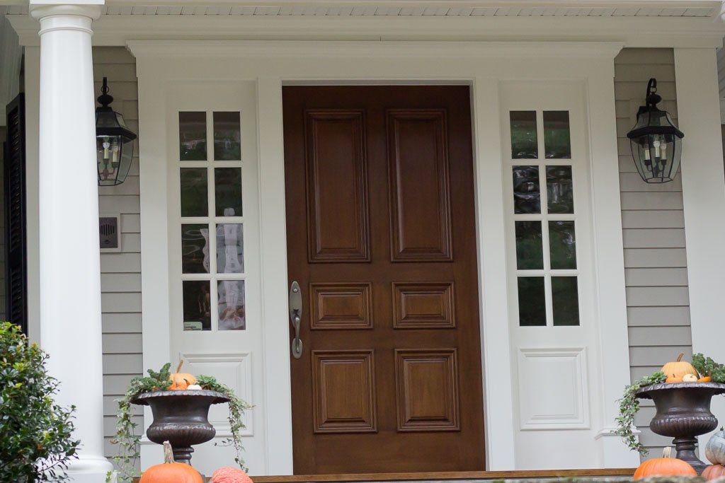 Front porch with a wooden door, white trim, and two wall lanterns flanking the entrance.