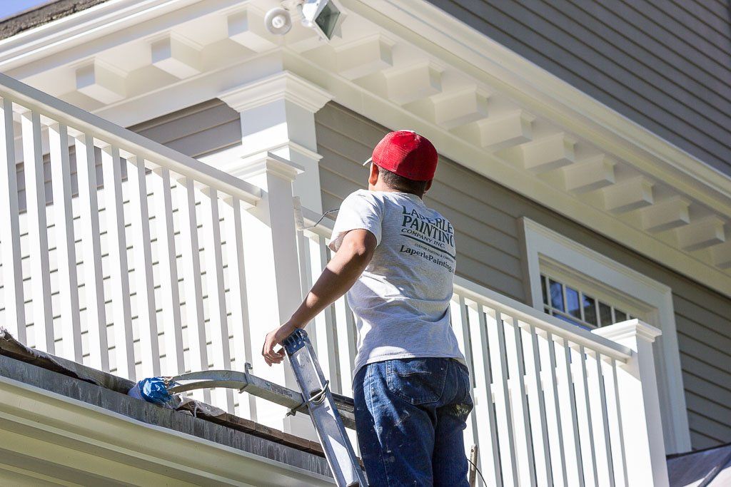Worker painting a white house exterior with a roller on a ladder