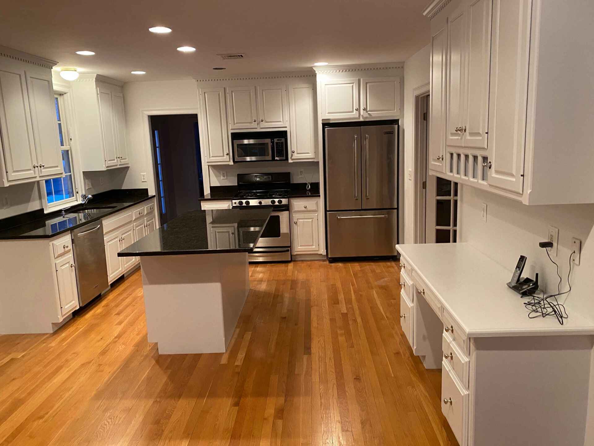 Bright modern kitchen with wood floors, white cabinets, black countertops, and stainless steel appliances