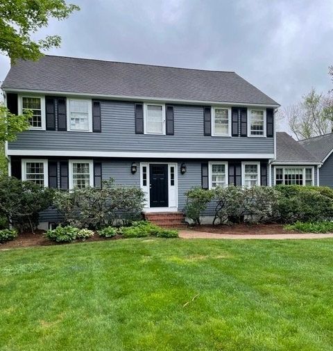 Two-story gray suburban house with white trim, black shutters, and a green front lawn