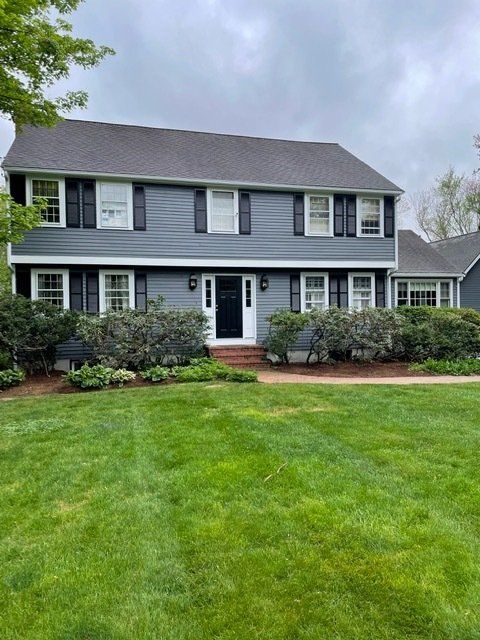 Two-story gray house with white trim and a green lawn under an overcast sky