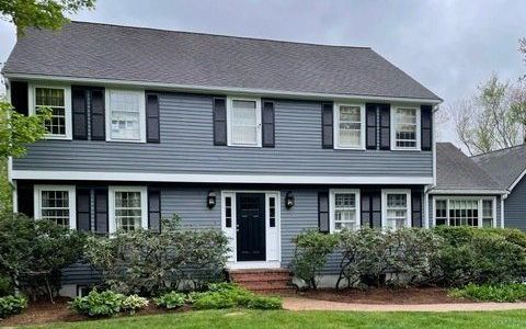 Two-story gray house with black shutters, white trim, front porch, and landscaped yard