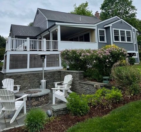 Gray house with white porch railings, stone patio, and garden landscaping on a sloped backyard.