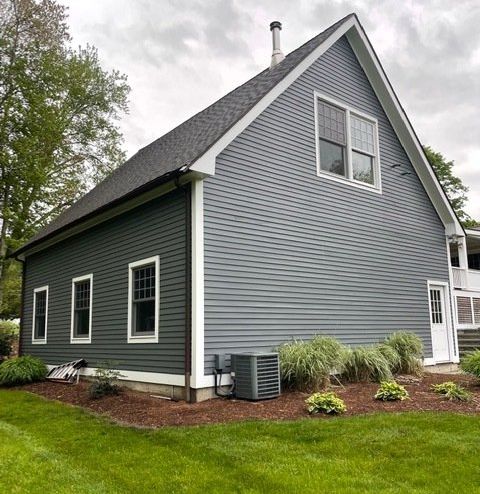 Gray and dark green house exterior with steep roof, white trim, and landscaped lawn