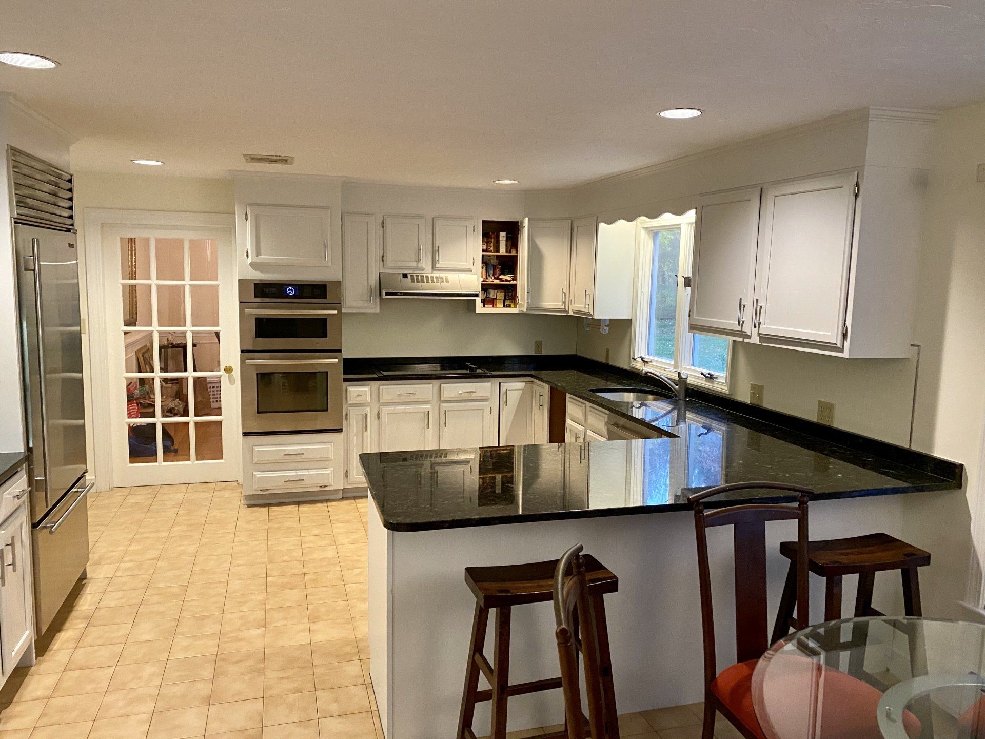 Bright white kitchen with black countertops, island stools, and built-in appliances