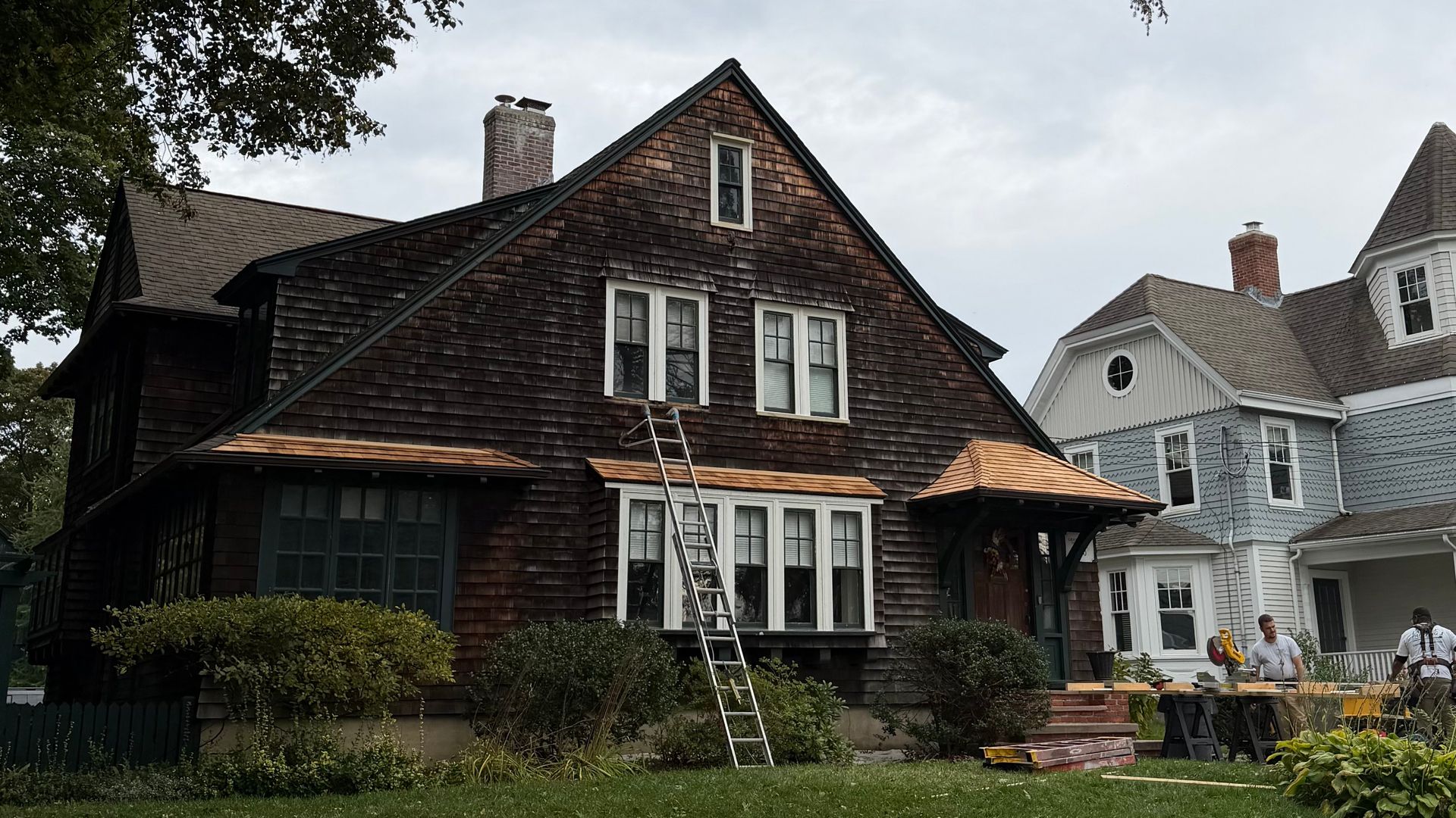 Dark brown shingled house in Medfield, MA with white-trimmed windows and a steep roof, surrounded by greenery.
