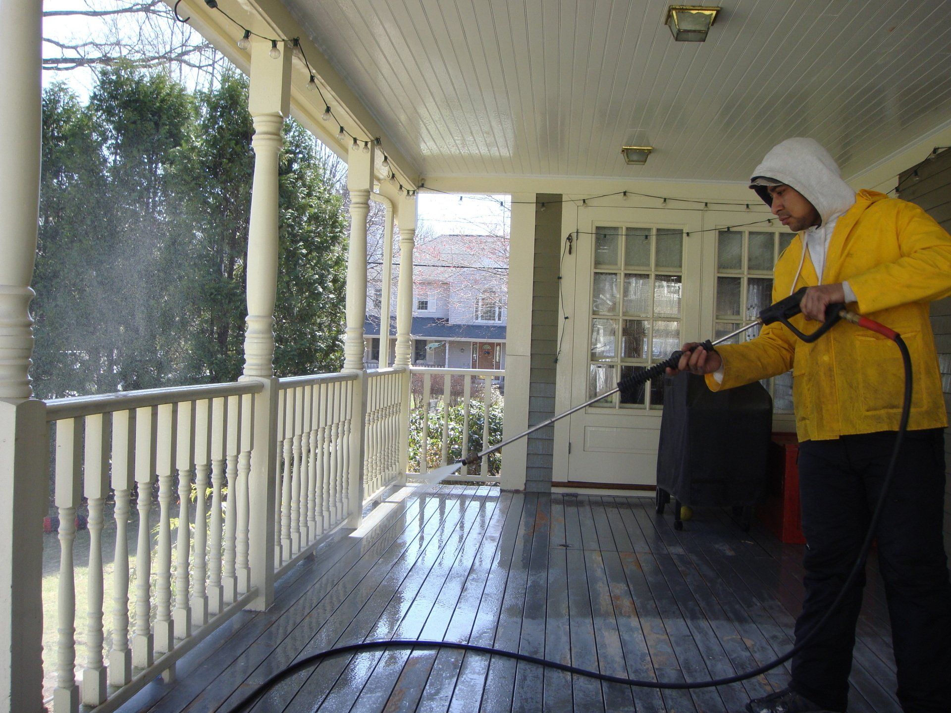 Person in a yellow jacket pressure washing a porch on a rainy day