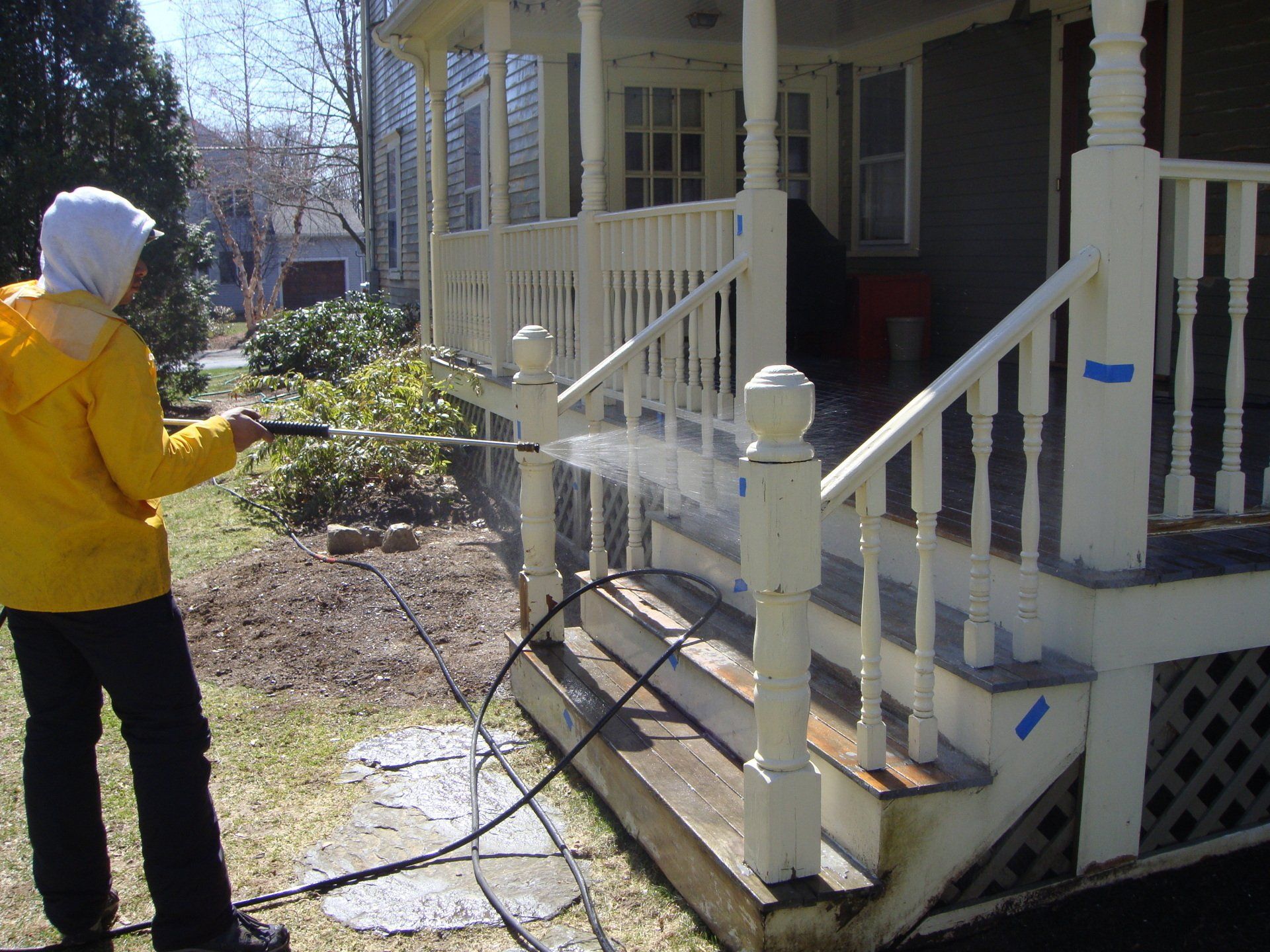 Person in a yellow jacket spraying a white porch with a hose outdoors