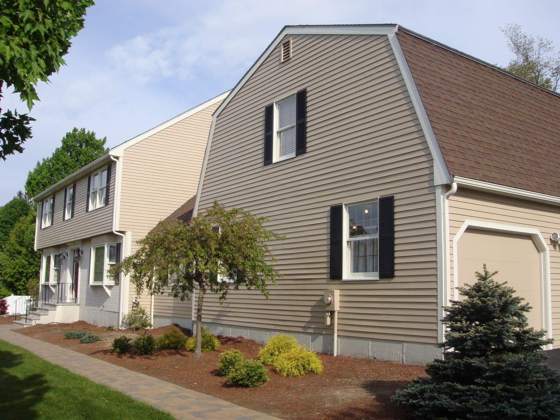 Suburban house with beige siding, brown roof, and small landscaped yard