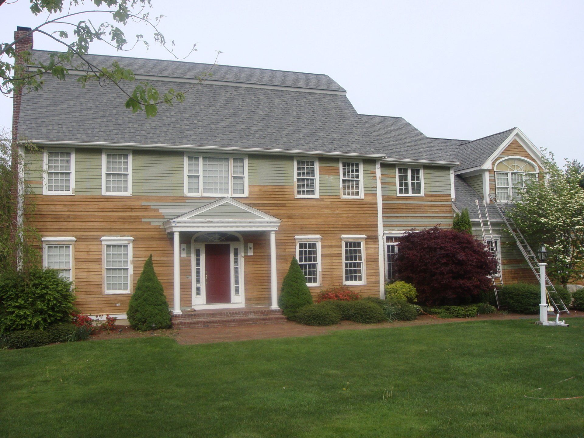 Large two-story suburban house with tan siding, gray roof, white trim, and a green lawn