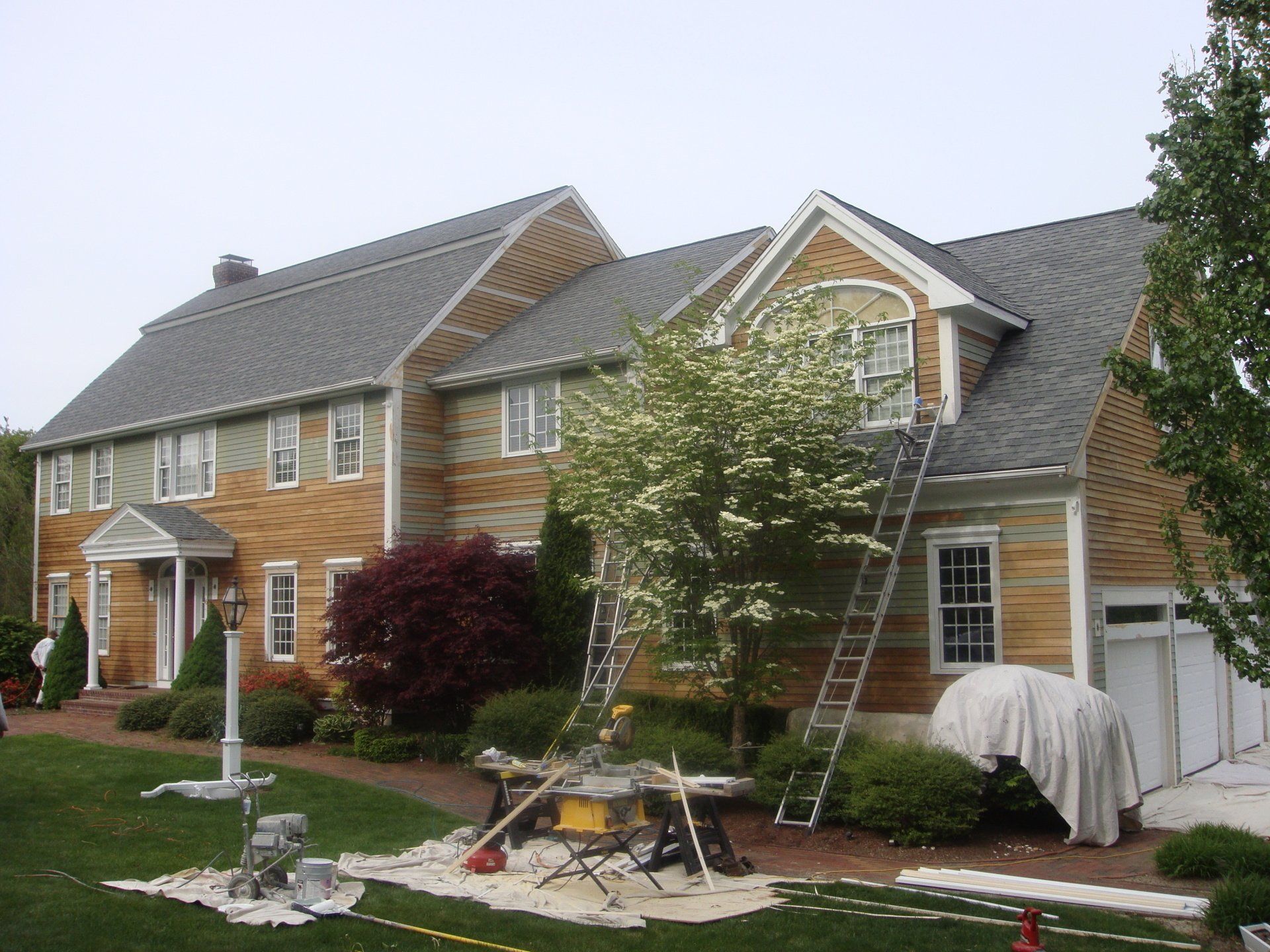 Suburban house with a ladder against the roof and landscaping tools in the front yard
